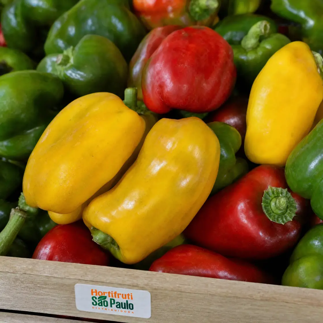 Close de pimentões amarelo, vermelho e verde com etiqueta Hortifruti São Paulo